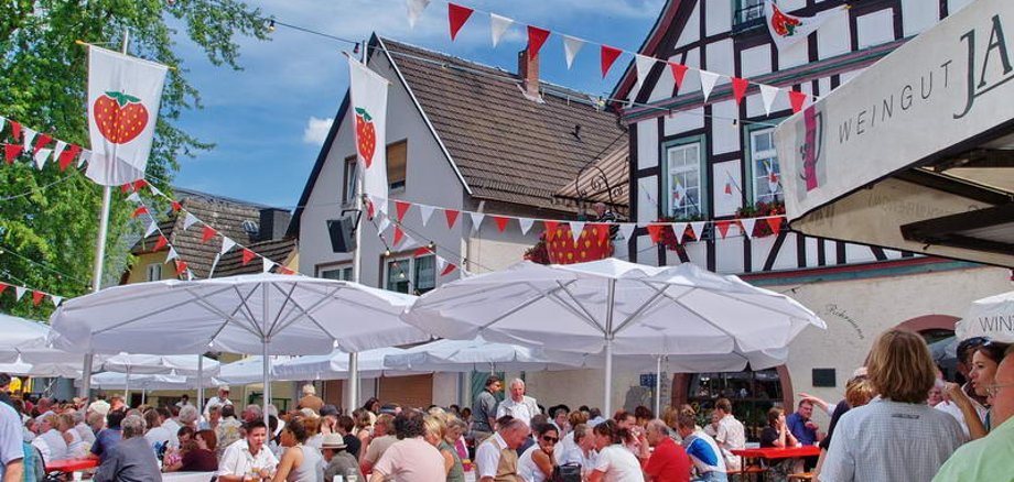 Viele Besucher sitzen auf Bierzeltgarnituren unter Sonnenschirmen auf dem Erbacher Marktplatz.
