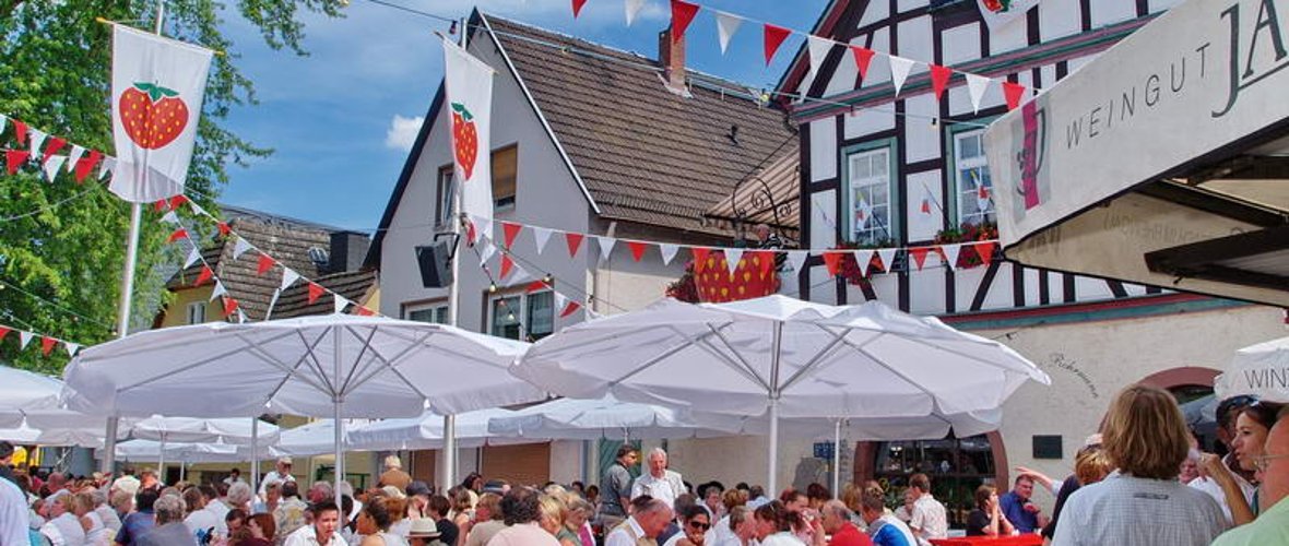 Das Erdbeerfest ist immer wieder ein Besuchermagnet. Viele Besucher sitzen auf Bierzeltgarnituren unter Sonnenschirmen auf dem Erbacher Marktplatz.