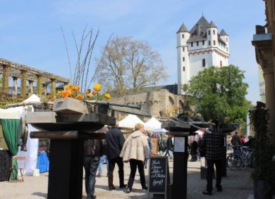 Menschen laufen an Ständen auf dem Leinpfad entlang, im Hintergrund sieht man die Eltviller Burg.