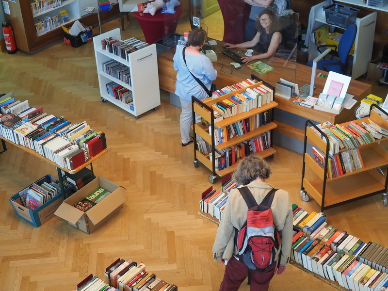 Bückerflohmarkt in der Mediathek: Eine Frau stöbert in den Büchern, eine andere Dame unterhält sich mit einer Mediatheksmitarbeiterin an der Ausleihe.