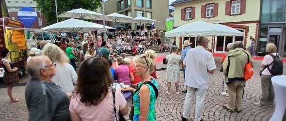 Menschen tummeln sich auf dem Platz vor der Mediathek an Stehtischen, Sitzstufen und unter Sonnenschirmen