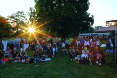 Publikum sitzt auf der Wiese, im Hintergrund scheint die Sonne durch die Bäume.