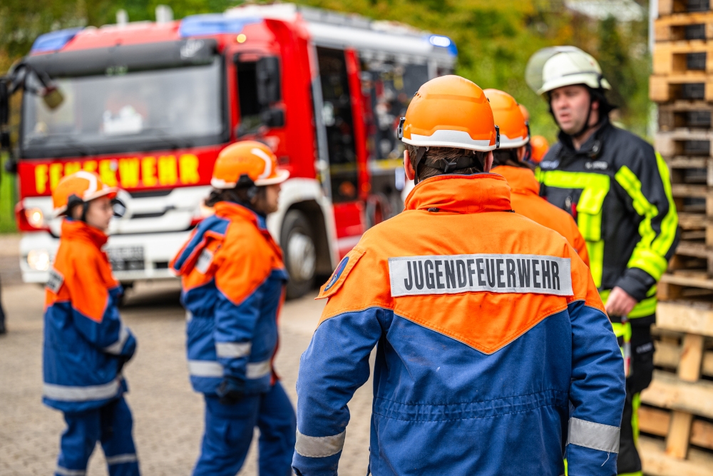 Mehrere Jungendliche in Ausrüstung von hinten zu sehen, im Hintergrund steht ein Feuerwehrauto