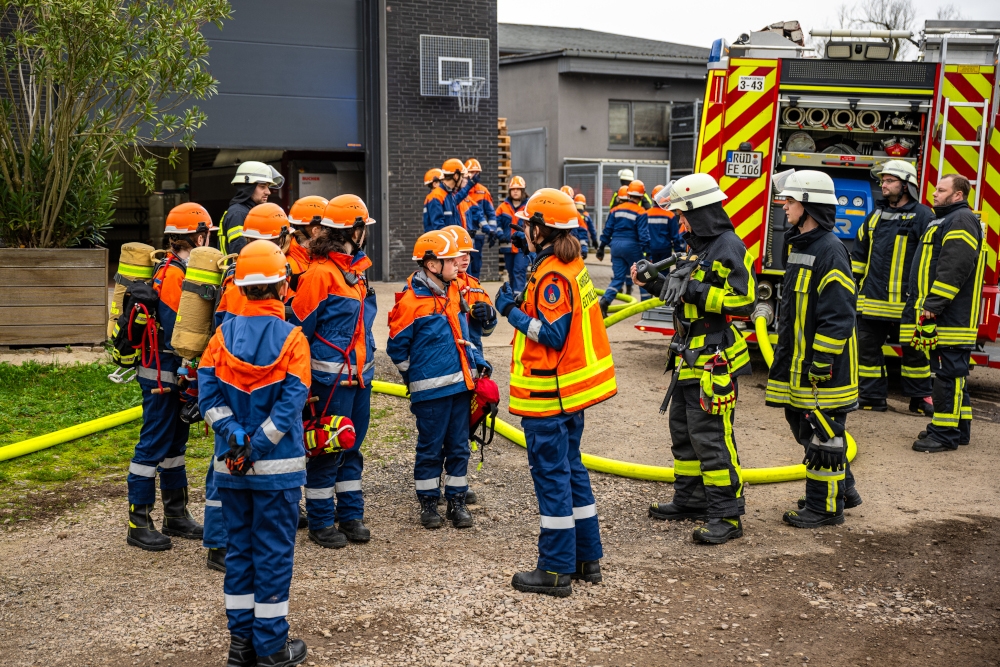 Viele Jugendliche und Erwachsene Feuerwehrleute vor einer Lagerhalle bei der Lagebesprechung