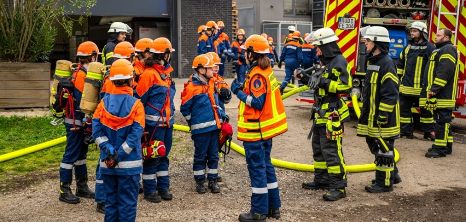 Viele Jugendliche und Erwachsene Feuerwehrleute vor einer Lagerhalle bei der Lagebesprechung