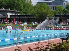 Immer was los im Eltviller Rosenbad. Schwimmerbecken mit rot-weißen-Fähnchen dekoriert. Im Hintergrund sieht man die Freibad-Rutsche und Personen, die im Wasser sind oder auf der Liegewiese entspannen.