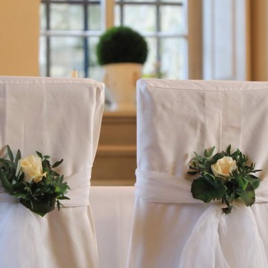 Nahaufnahme von zwei weiß bezognen Stühlen, die mit weißen Rosengestecken geschmückt sind.