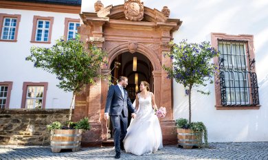 Brautpaar kommt Hand in Hand durch einen Torbogen ins Freie.