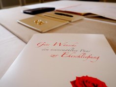 Zur Eheschließung wünschen wir Ihnen nur das Beste. Eine Mappe mit Trauunterlagen, im Hintergrund liegen zwei Eheringe.