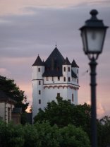 Abendlicht hüllt den Burgturm ein. Burgturm der Kurfürstlichen Burg in der Dämmerung, rechts sieht man eine Straßenlaterne.