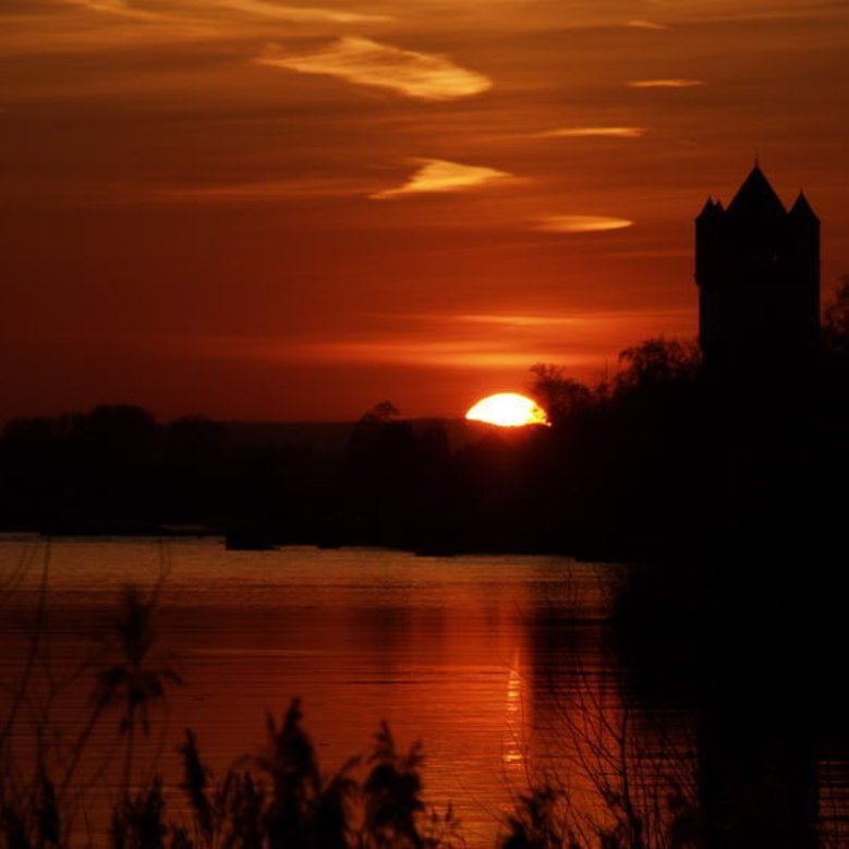 Sonnenuntergang am Rheinufer mit der Silhouette der Burg.
