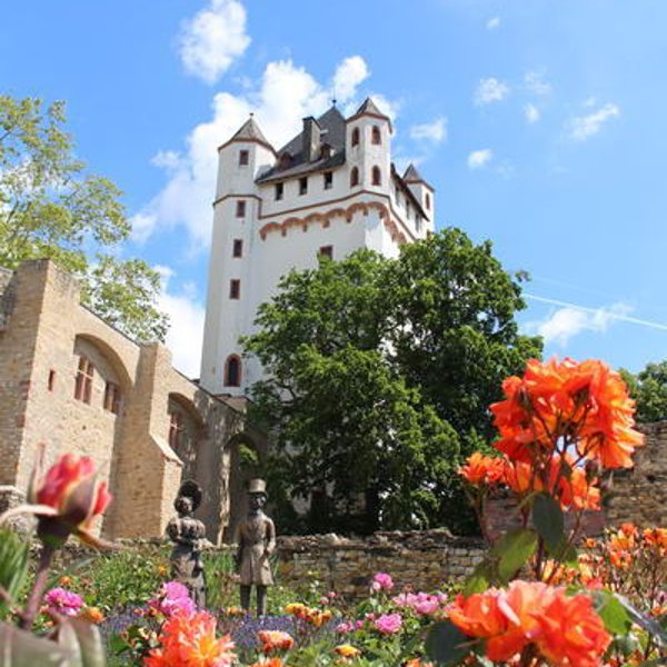 Blühende organgene Rosen mit Biedermeierfiguren, Rosenbeet und Burgturm im Hintergrund.