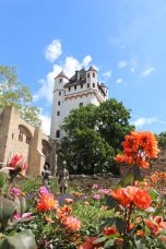 Blühende organgene Rosen mit Biedermeierfiguren, Rosenbeet und Burgturm im Hintergrund.