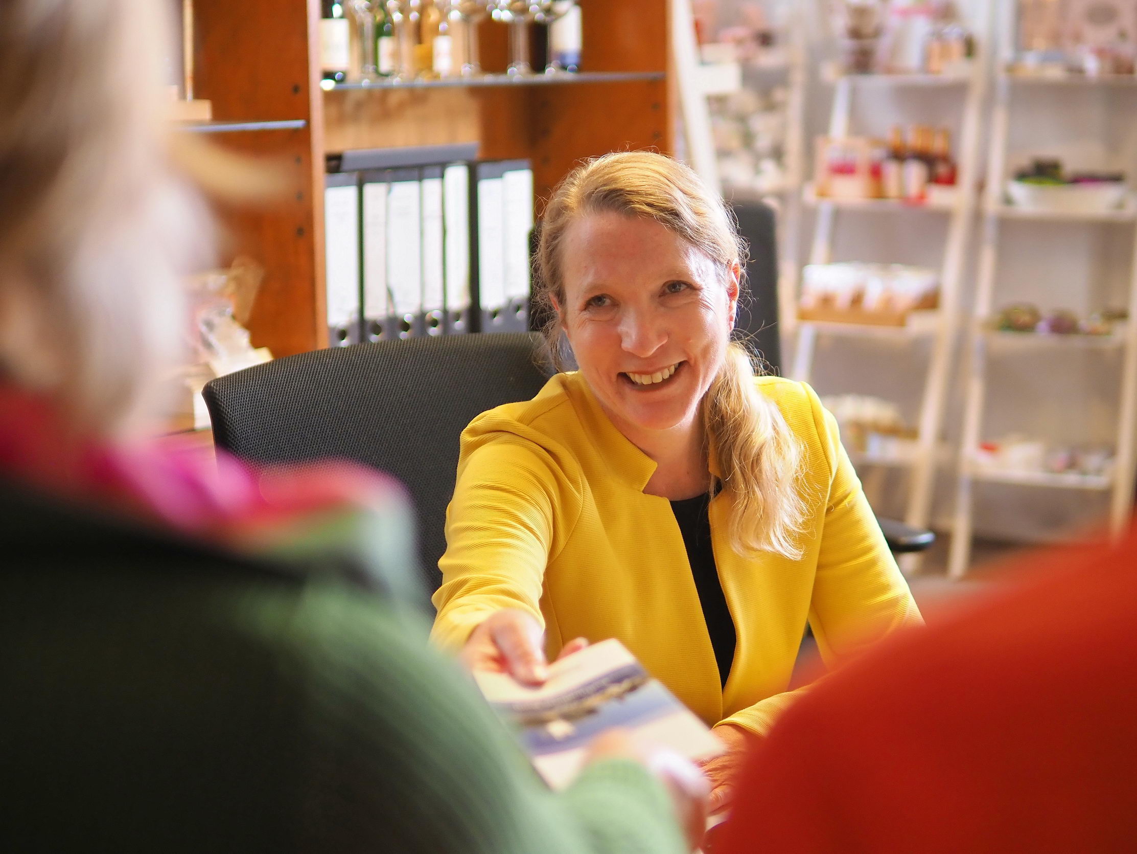 Eine Mitarbeiterin der Tourist-Info berät eine Besucherin, über deren Schulter das Bild aufgenommen wurde.