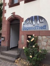 Eingang Jugendzentrum: Vor dem Eingang blühen Rosen und es hängt ein Schild "Eltviller Jugendzentrum" am Gebäude.