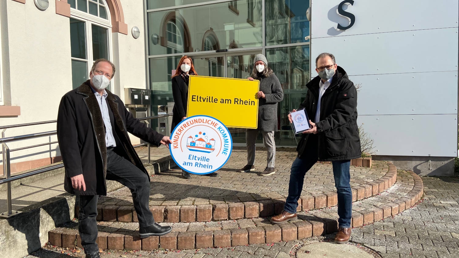 Stadtverordnetenvorsteher Ingo Schon, Jugendpflegerin Franziska Bruns, Kinder- und Jugendbeauftragte Ursula Wolf und Bürgermeister Patrick Kunkel freuen sich über die Auszeichnung. Stadtverordnetenvorsteher Ingo Schon, Jugendpflegerin Franziska Bruns, Kinder- und Jugendbeauftragte Ursula Wolf und Bürgermeister Patrick Kunkel stehen vor dem Rathaus und halten das Siegel sowie ein Ortsschild.