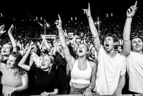 Schwarzt-weiß-Fotografie von jubelnden und singenden Menschen auf einem Konzert in der 1. Reihe.