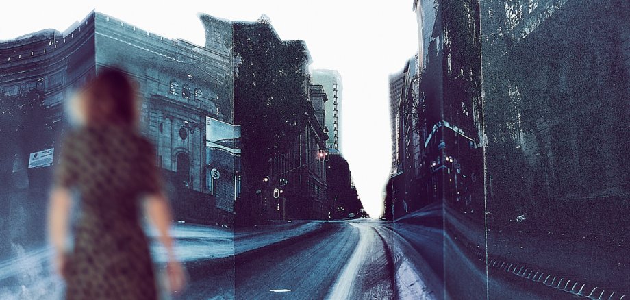Dunkle Fotografie einer Straße mit Gebäuden, links ist eine Frau von hinten zu sehen, die sich vorwärts bewegt. Das Bild ist leicht verschwommen.