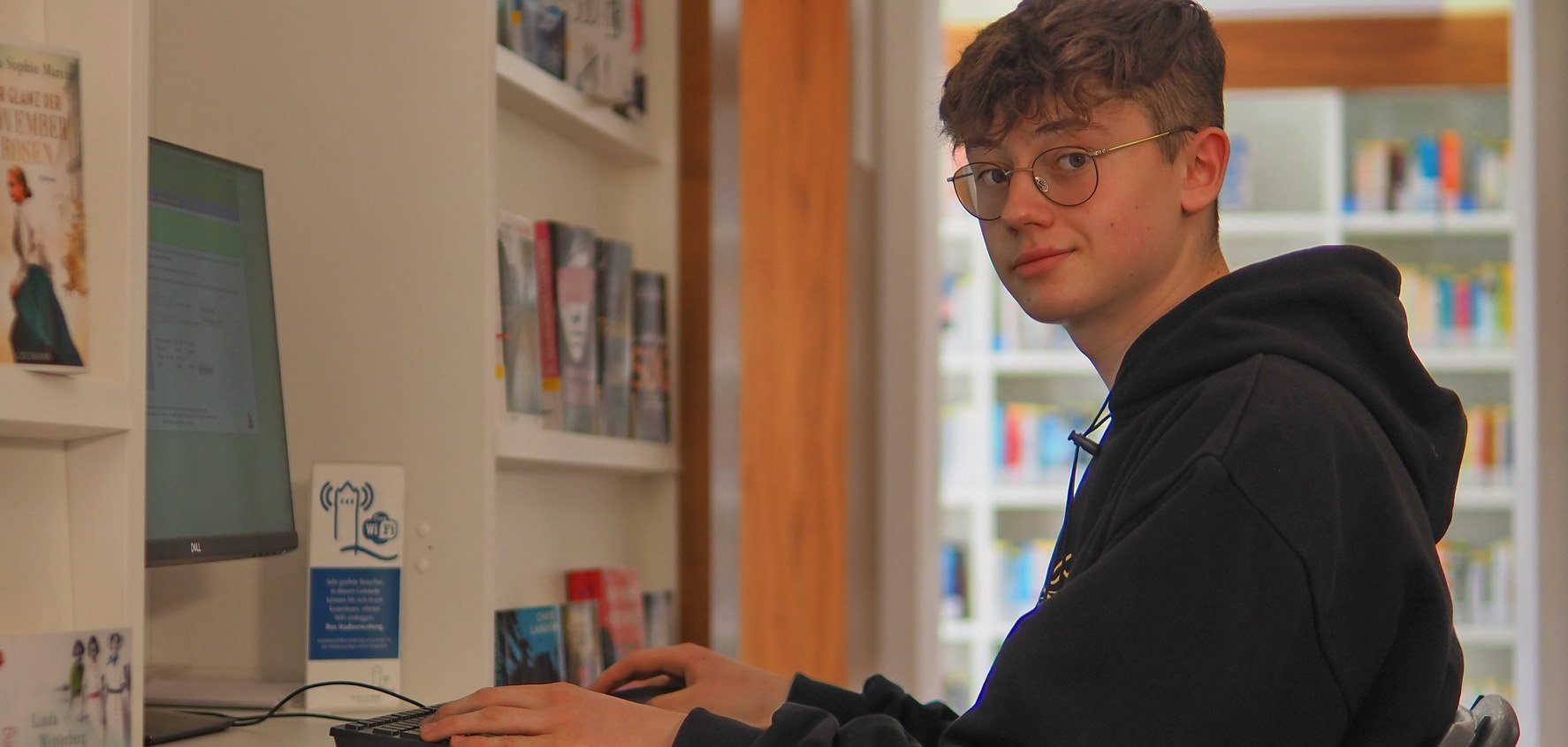 Ein Jugendlicher schaut in die Kamera und sitzt vor einem Computer.