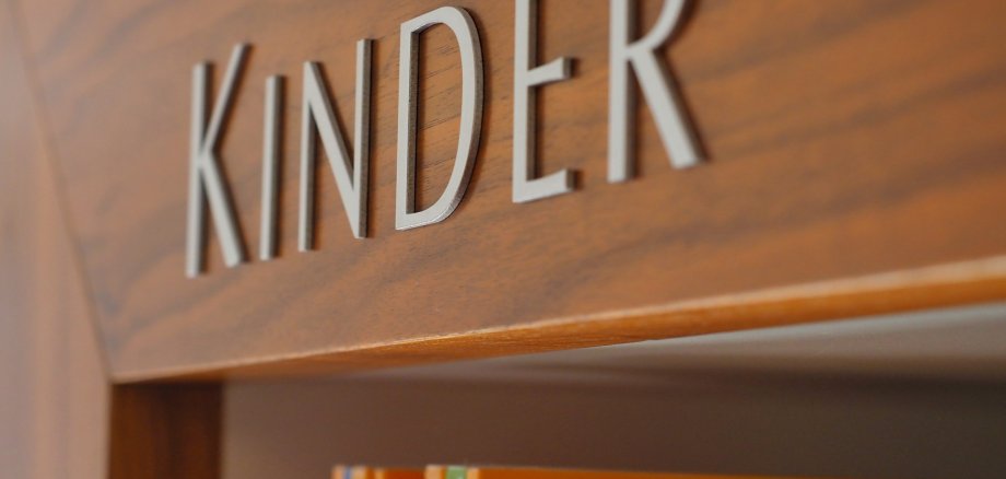 An einem Bücherregal steht "Kinder".