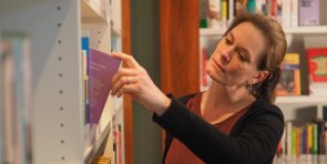 Die Mediathek lädt zum Stöbern und Entdecken ein. Eine Besucherin der Mediathek zieht ein Buch aus einem Regal und betrachtet es.