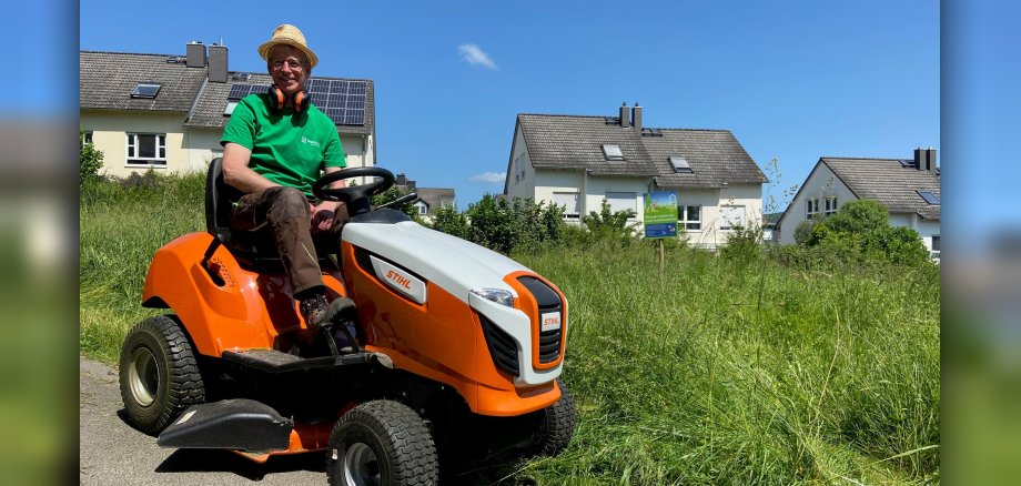 Friedhofsgärtner Matthias Bleul sitzt auf einem Rasenmäher-Traktor am Rande einer Blühwiese.
