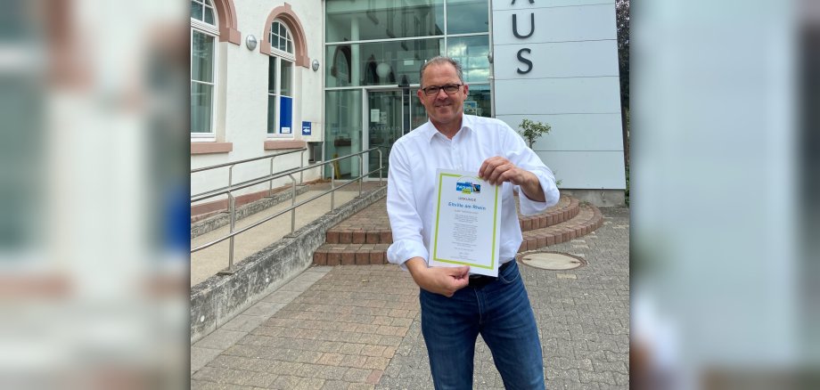 Bürgermeister Kunkel steht mit der Urkunde Fairtrade-Town vor dem Rathaus in Eltville.