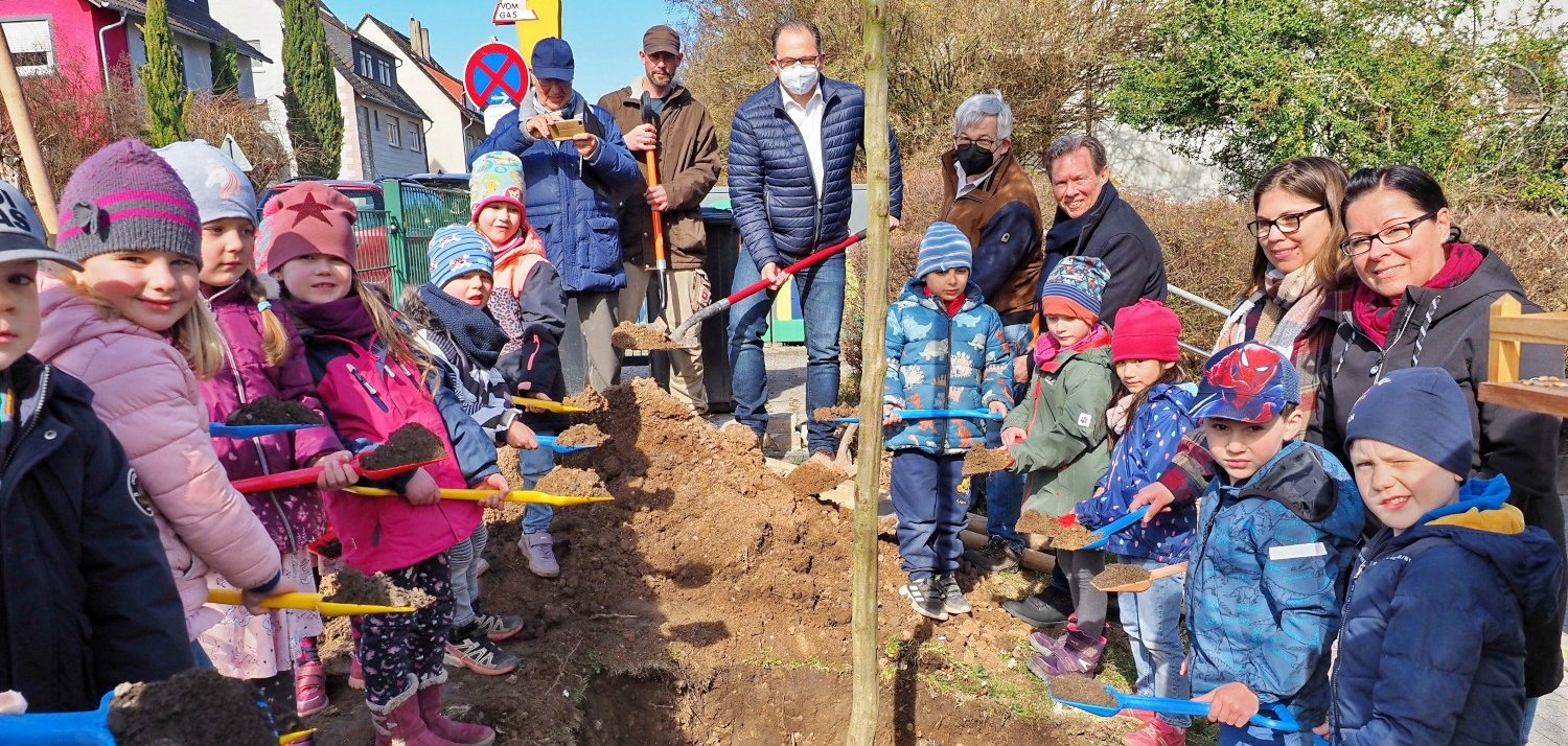 Kinder der KITA Wichtelhäuschen in Hattenheim, Volker Ostermann, Jürgen Fuchs und Ernst von Voigt vom Kiwanisclub, Steffen Conrad vom Fachbereich Grünpflege, Dany Kopp und Angelique Beauchez von der KITA sowie Bürgermeister Patrick Kunkel pflanzen einen neuen Baum.