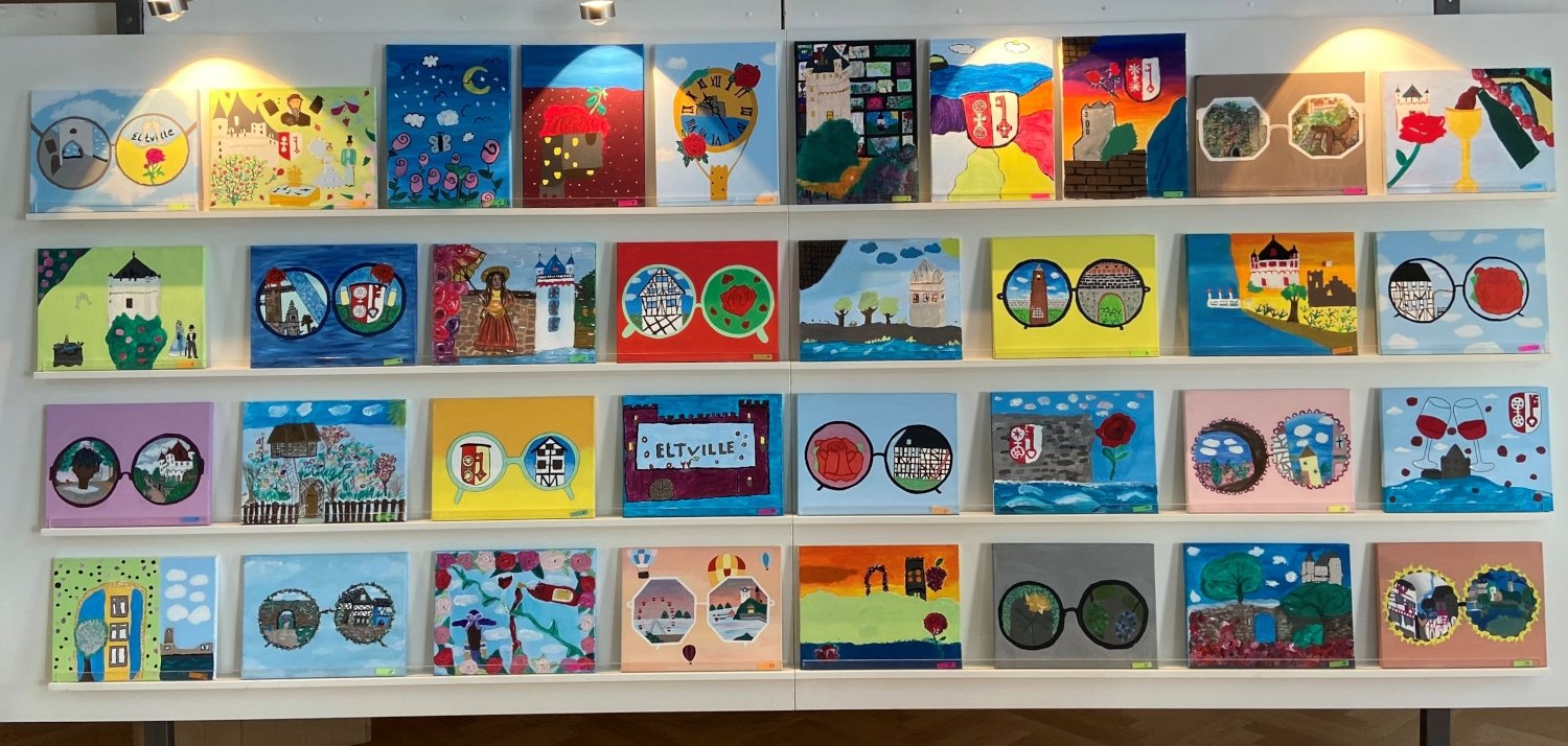 Die gemalten Bilder stehen aufgereiht in einem Ausstellungsregal in der Mediathek.