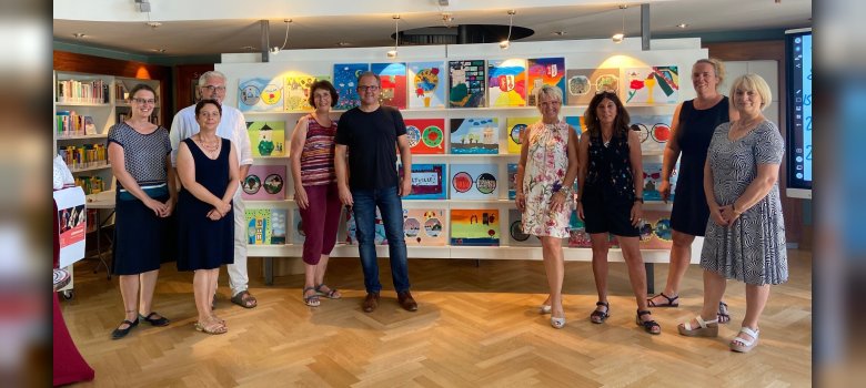Jury für die Auswahl der Motive Die Jury aus Bürgermeister und Mitarbeitenden der Stadtverwaltung, Vertretern des Handels, des Fairtrade Steuerungskreises und der Realschule vor den gemalten Motiven der Realschüler, die in der Mediathek aufgestellt wurden.