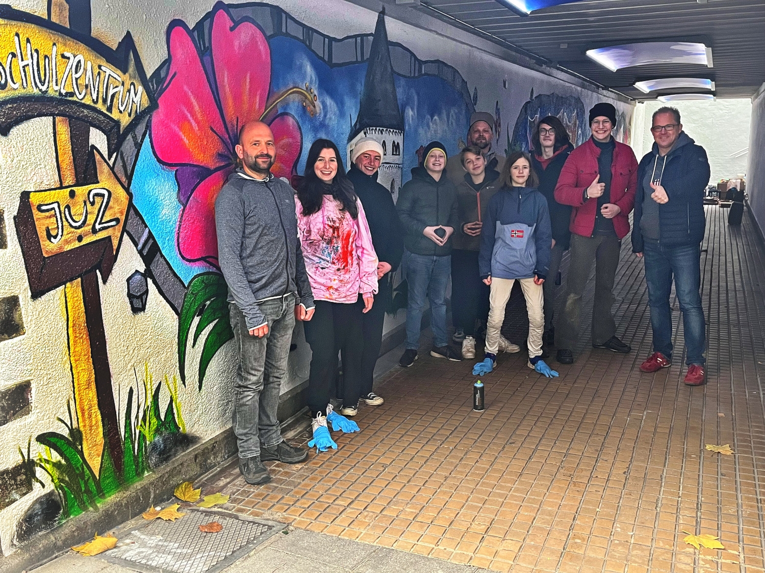 Ortsvorsteher Markus Post und Bürgermeister Patrick Kunkel mit dem Graffitikünstler und den Jugendlichen aus dem KJB in der Unterführung vor ihrem Sprühkunstwerk.