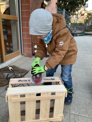 Ein Junge schleift eine Holzkiste ab.