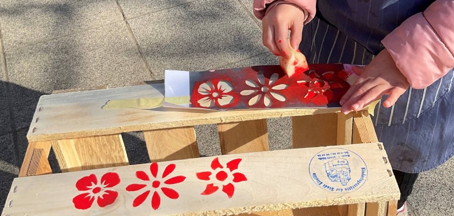 Kinderhände stempeln rote Blumen auf eine kleine Holzkiste.