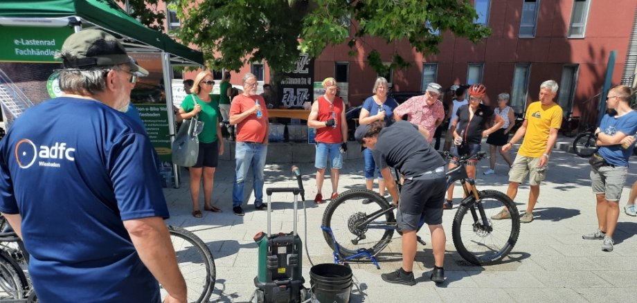 Interessierte stehen im Halbkreis und schauen dem Experten beim Fahrradreinigen zu.
