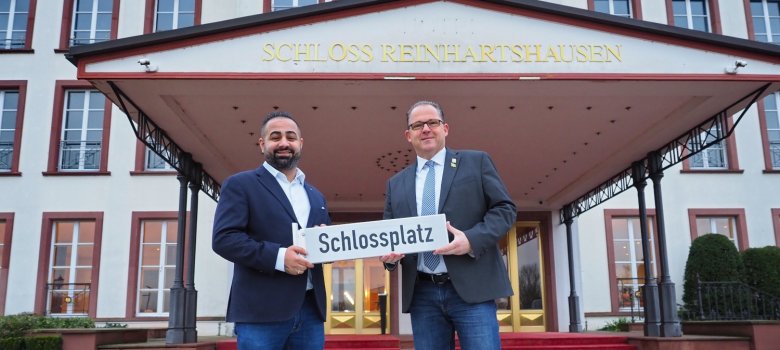 Bürgermeister und Geschäftsführer vom Schloss mit dem Straßenschild in der Hand vor dem Schlosseingang