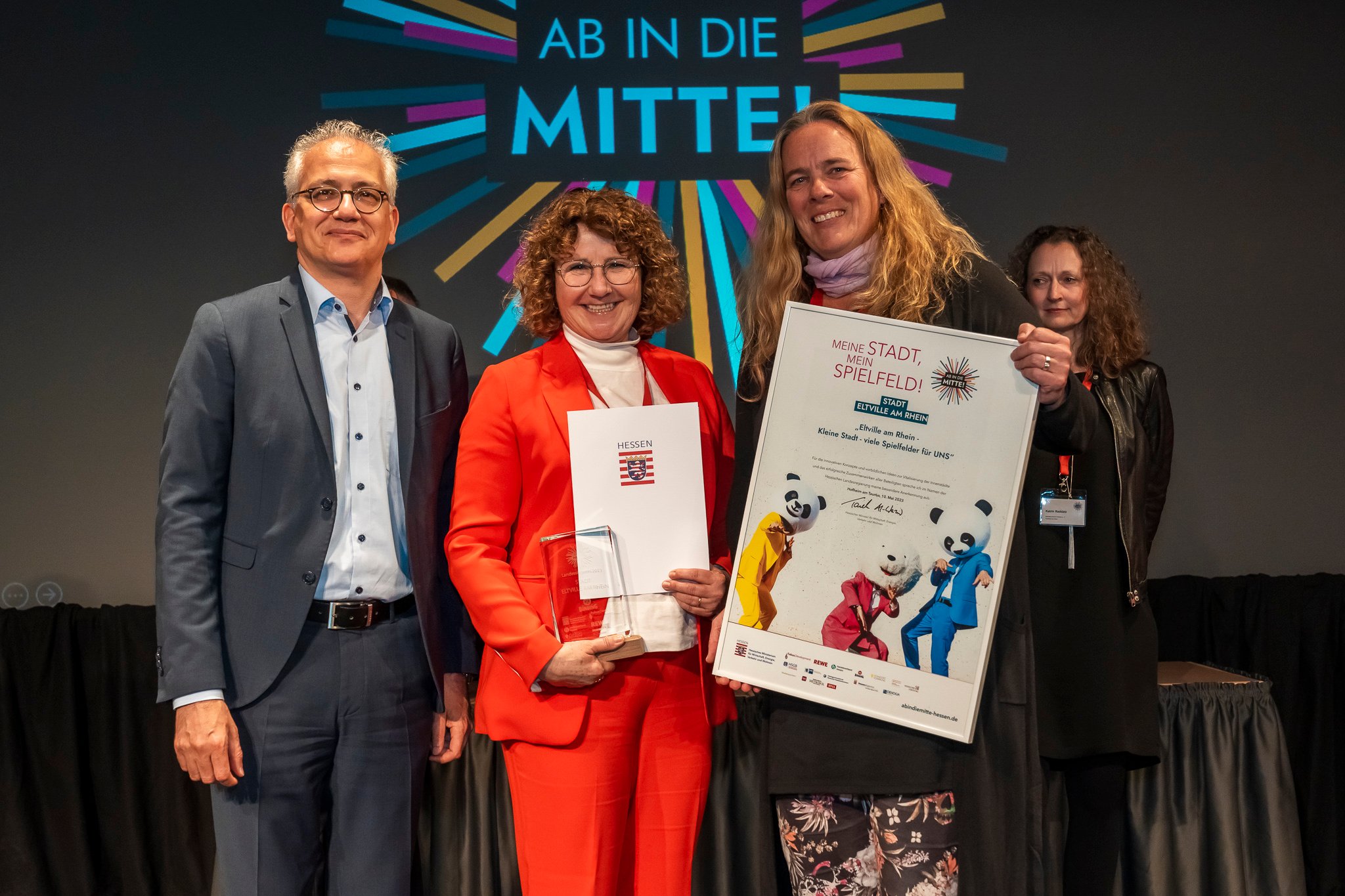 Gaby Roncarati von der Philipp Kraft Stiftung (Mitte) und Inga Olze vom Team der Stadt Eltville am Rhein nehmen den Preis beim hessischen Innenstadt-Wettbewerb „Ab in die Mitte“ aus den Händen von Wirtschaftsminister Tarek Al-Wazir entgegen.