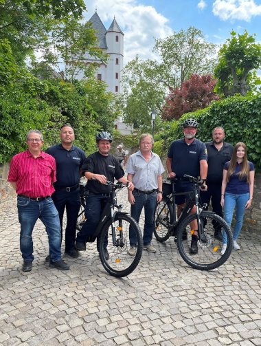 Gruppenfoto: Die Mitarbeiter der Ordnungspolizei, Erster Stadtrat Hans-Walter Pnischeck, Ordnungsamtsleiter Markus Wolf und seine Vertreterin Tamara Mathiowetz mit den neuen Diensträdern vor der Eltviller Kurüfrstlichen Burg.