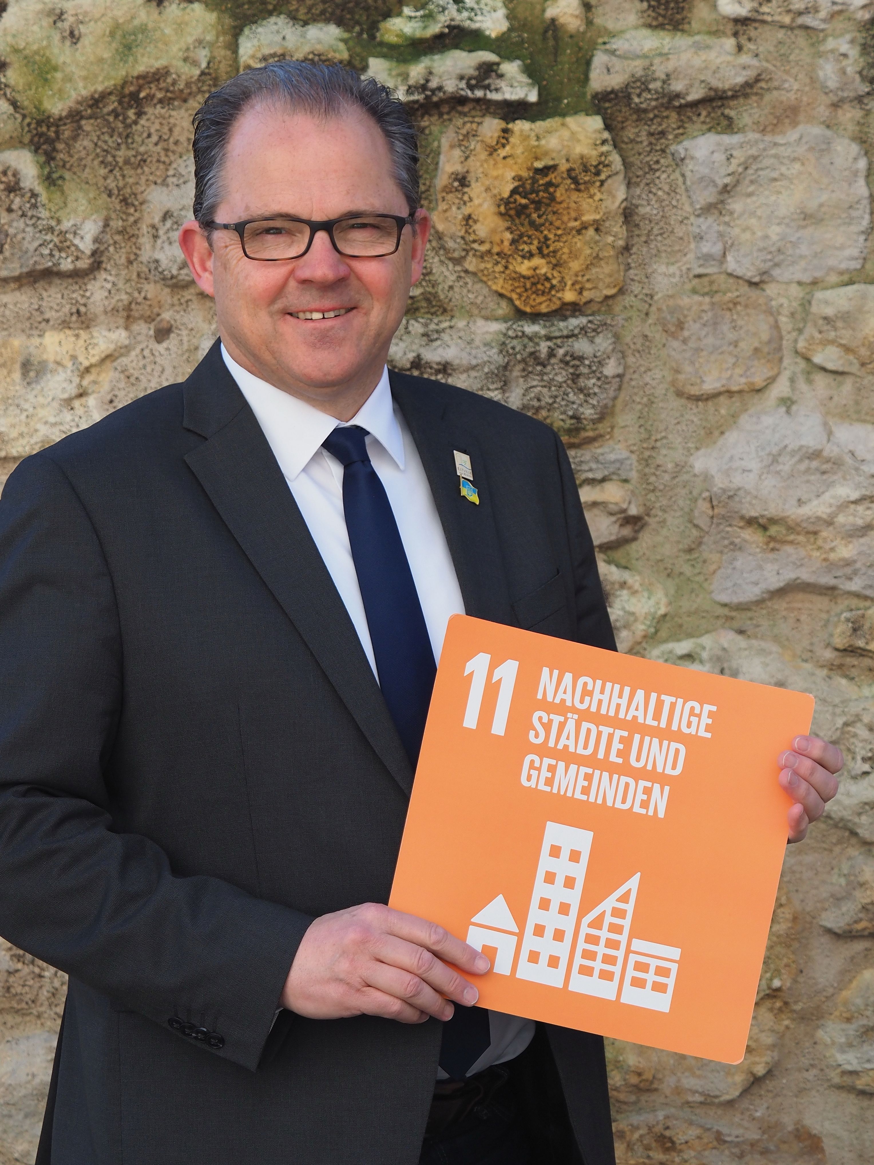 Bürgermeister Kunkel hät ein Schild, das das Ziel 11 Nachhaltige Städte und Gemeinden zeigt