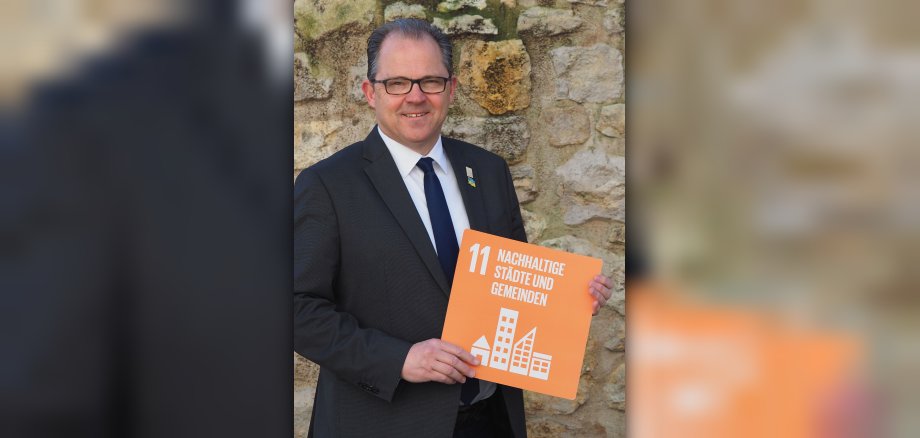 Bürgermeister Kunkel hät ein Schild, das das Ziel 11 Nachhaltige Städte und Gemeinden zeigt
