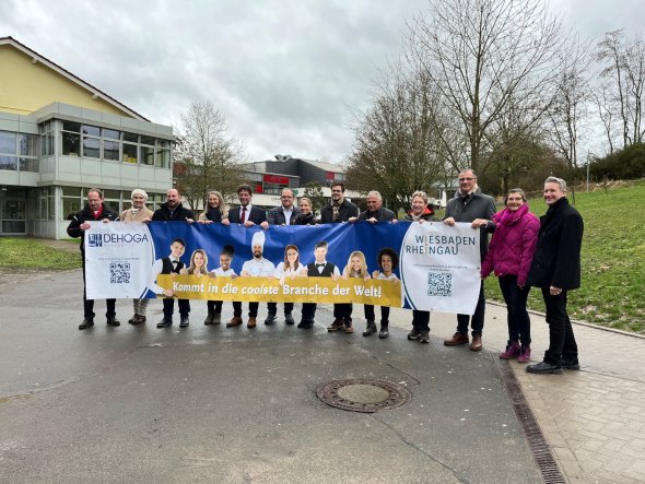 Mitglieder des Runden Tisches "Arbeitskräftemangel Rheingau" sowie Vertreter der Rheingauer Kommunen und des Dehoga bringen ein Banner zur Kampagne "Arbeitskräftegewinnung" zum Eltviller Schulzentrum.