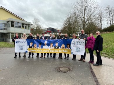 Mitglieder des Runden Tisches "Arbeitskräftemangel Rheingau" sowie Vertreter der Rheingauer Kommunen und des Dehoga bringen ein Banner zur Kampagne "Arbeitskräftegewinnung" zum Eltviller Schulzentrum.