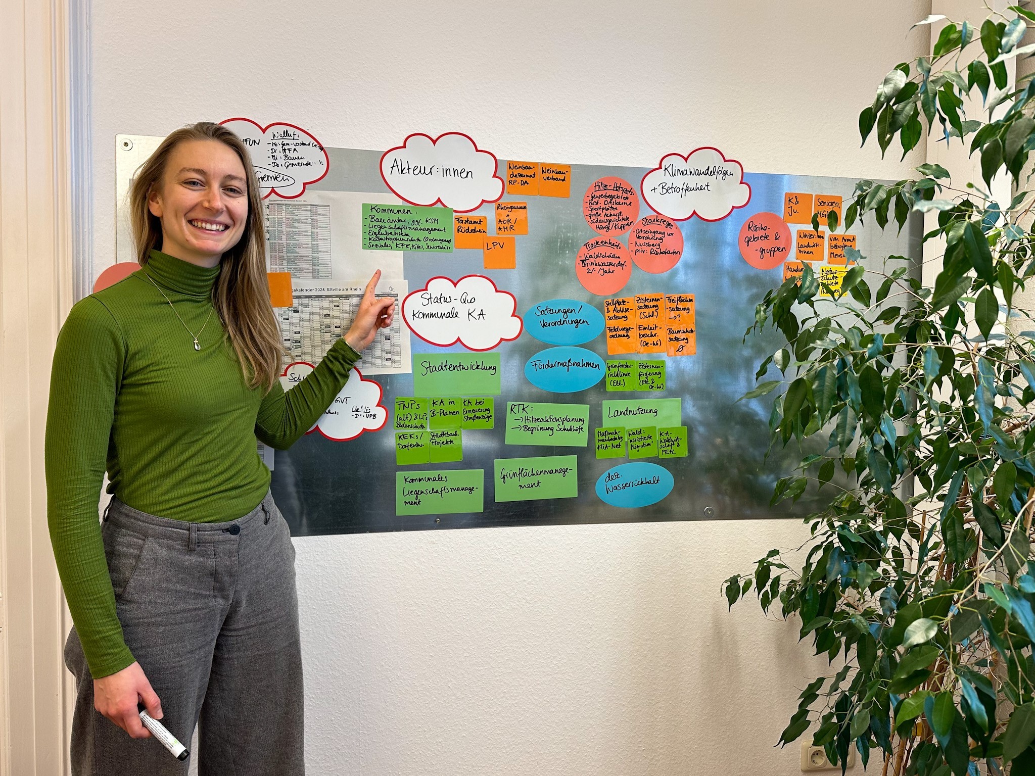 Hannah Fröb zeigt auf bunte beschriftete Zettel an einer Pinnwand