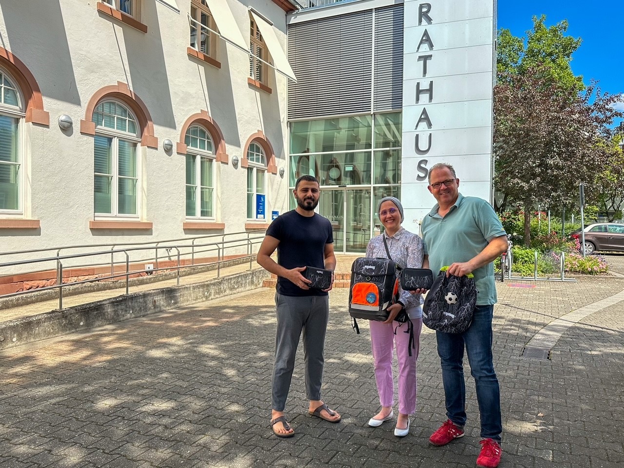 Bürgermeister mit dem Ehepaar Hussein vor dem Rathaus mit Schulranzen in der Hand