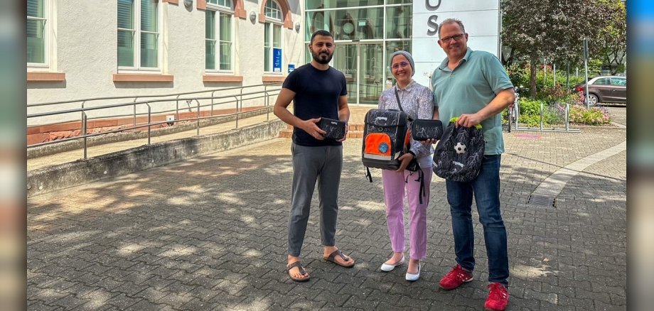 Bürgermeister mit dem Ehepaar Hussein vor dem Rathaus mit Schulranzen in der Hand