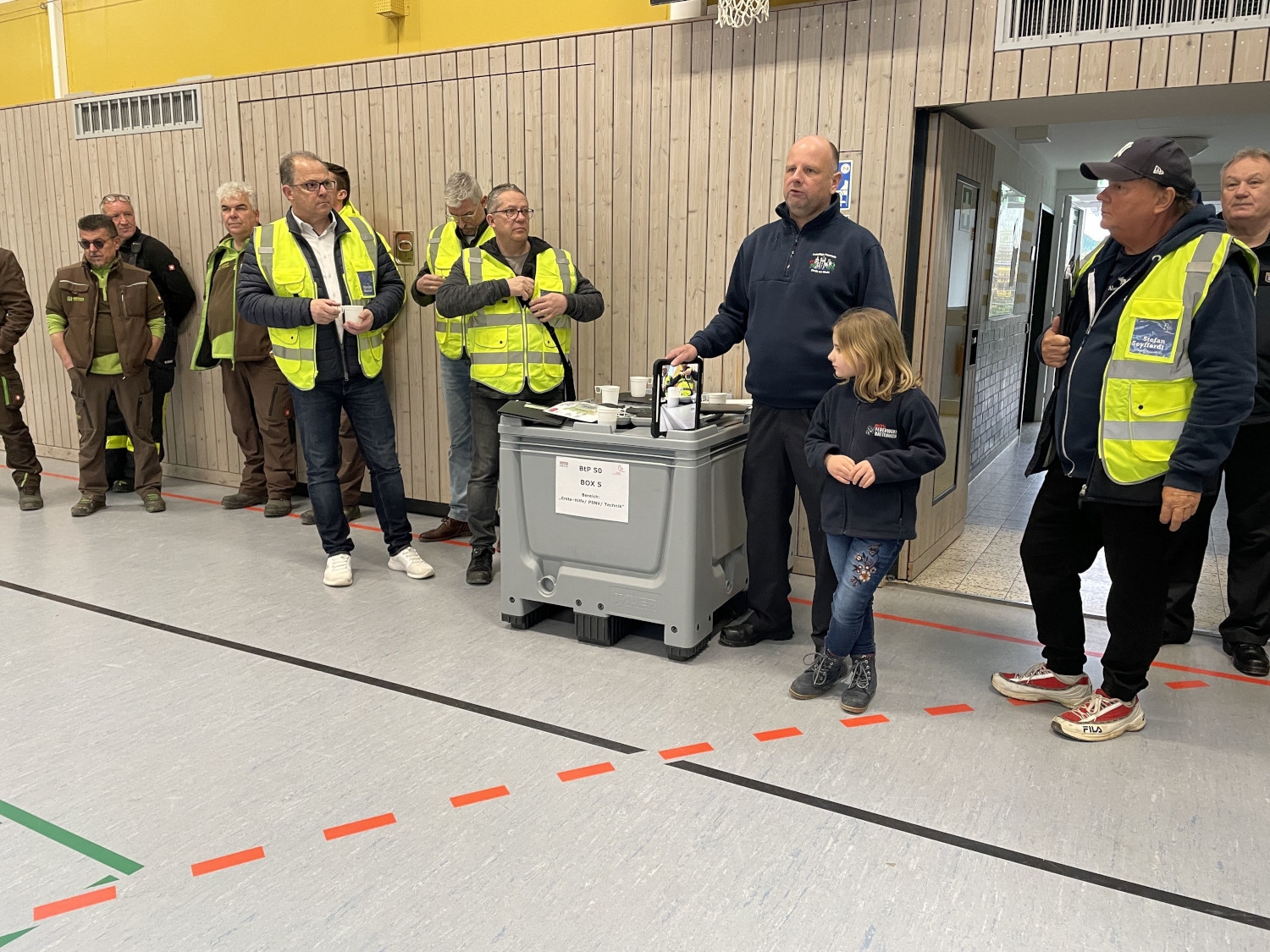 Bürgermeister und Beteiligte stehen mit Warnwesten in der Turnhalle bei der Lagebesprechung