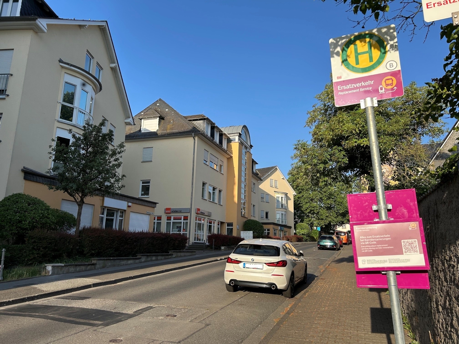 Eine Bushaltestelle an einer Straße, im Hintergrund fährt ein Auto.