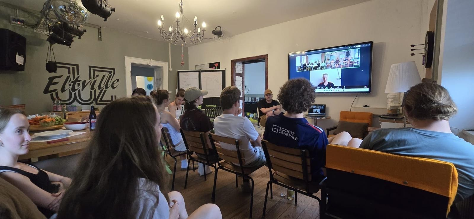 Jugendliche im Jugendzentrum Eltville schauen im Rahmen einer Videokonferenz auf einen Bildschirm, der an der Wand hängt. Auf dem Bildschirm sieht man ukrainische Jugendliche.