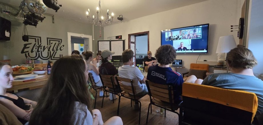 Jugendliche im Jugendzentrum Eltville schauen im Rahmen einer Videokonferenz auf einen Bildschirm, der an der Wand hängt. Auf dem Bildschirm sieht man ukrainische Jugendliche.