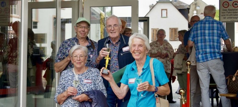 2  Damen und 2 Herren stehen neben einem Stehtisch. Eine der Damen hält eine Oscarfigur in der Hand, auf dem Tisch steht eine Flasche Sekt.