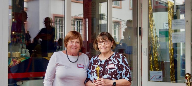 2 Damen stehen vor einem Kino. Neben ihnen ein Stehtisch mit Sektflaschen und Sektgläsern.